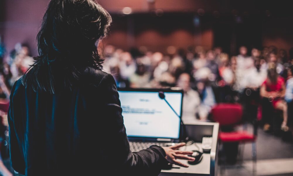 Speaker delivering a clear and confident message at an event, using a keynote microphone on stage to engage the audience effectively.