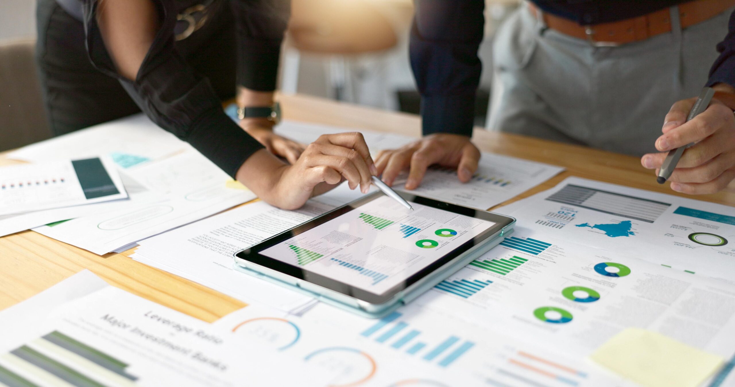 Group of people examining charts on an iPad and sheets of paper, holding a pen while measuring and discussing return on investment (ROI).