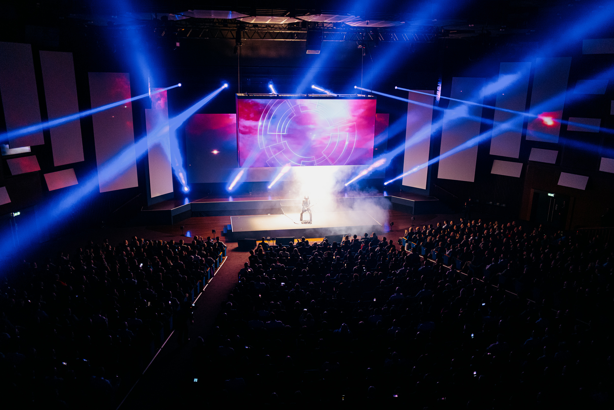 Guitarist performing on stage at a large-scale event with elaborate staging and a dynamic light show, designed to captivate the audience and create memorable moments