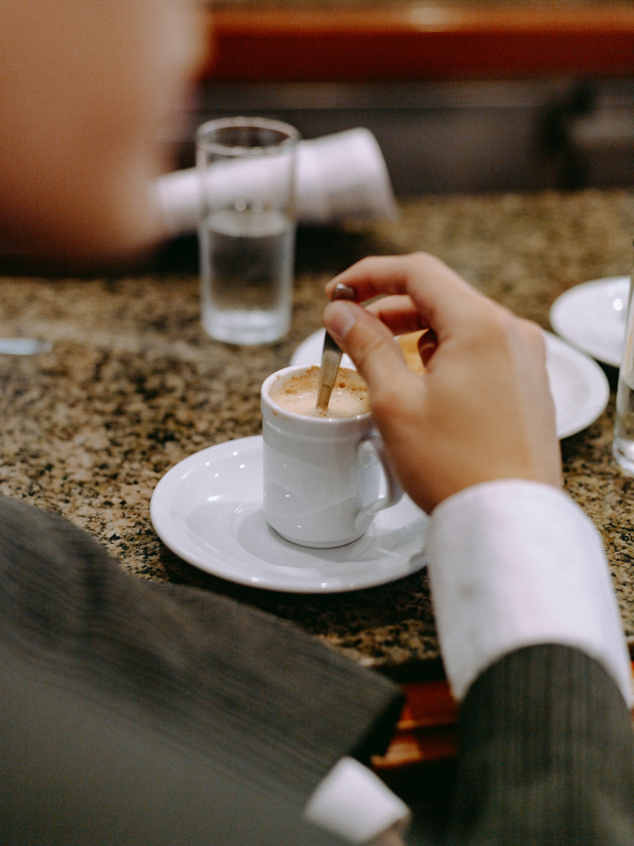 Person stirring a cup of coffee while engaging in conversation with a potential lead at an event