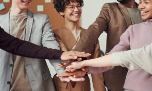 Team building event with colleagues putting their hands together in the centre to show unity and teamwork.