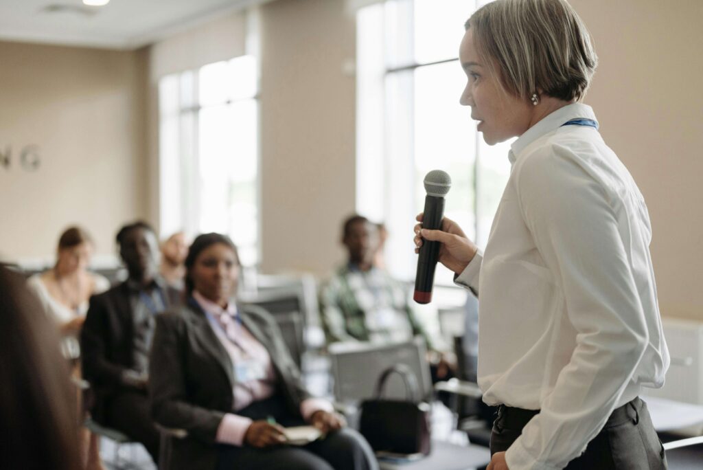 Confident woman speaking into a microphone in front of a small group, demonstrating strong public speaking skills.