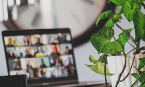 Employees in a modern office participating in a virtual meeting on a large screen, showcasing hybrid communication and internal collaboration between in-person and remote teams.