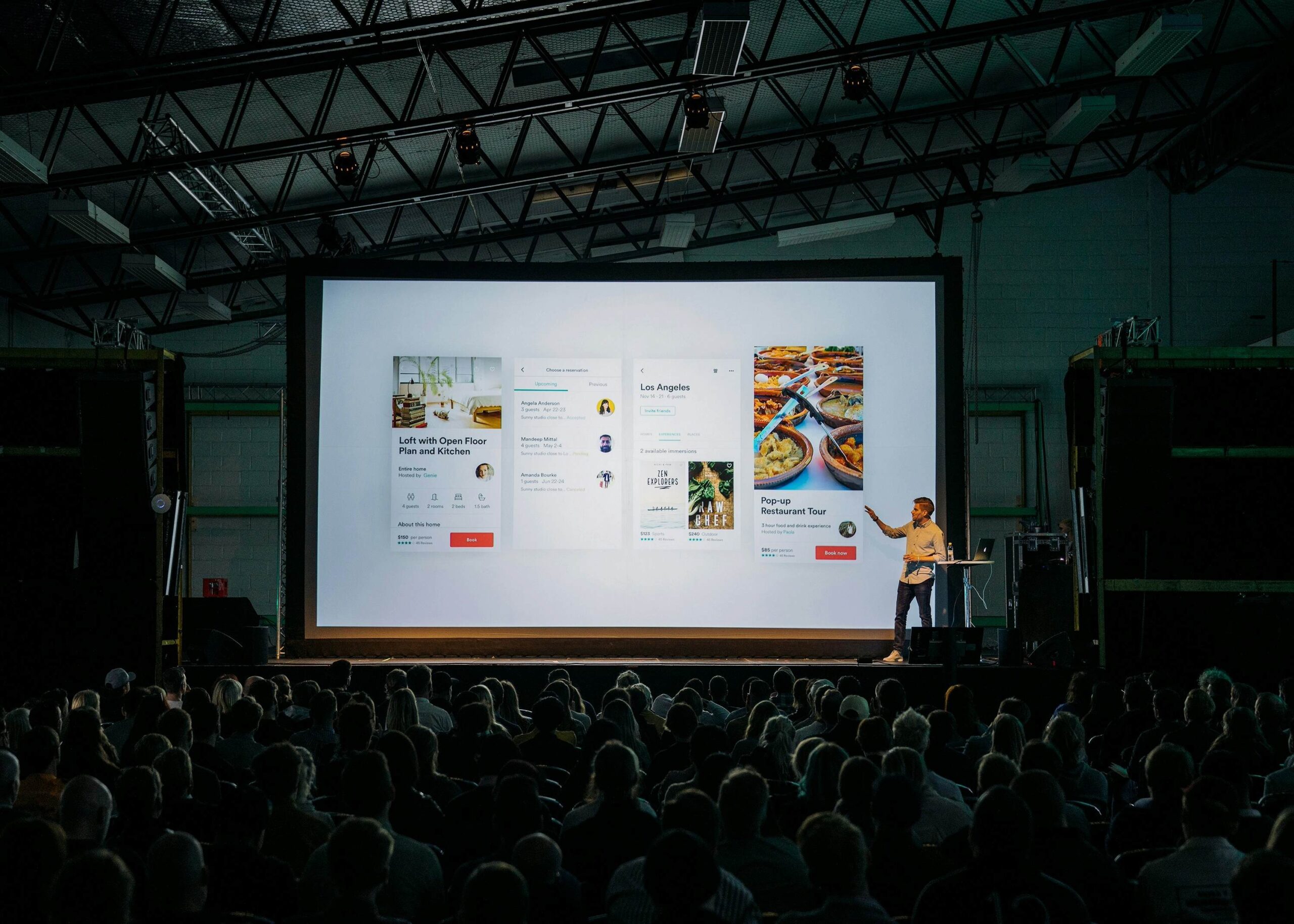 Conference speaker presenting on stage beside a large visual communication slide during a corporate leadership event.